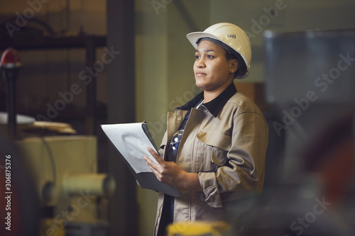 Waist up portrait of female foreman holding clipboard while supervising production at factory, copy space