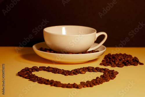 Heart shape made from coffee beans in front of a cup of coffee