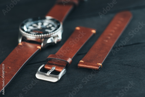 Brown leather handmade watch strap with steel buckle on men's luxury watch laying on dark rustic wooden table. 