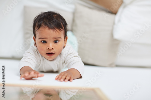 Cute baby girl with dark hair lying and playing on the floor