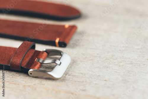 Brown leather handmade watch strap with steel buckle on rustic wooden surface. Closeup. Copy space.