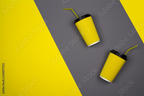 Yellow paper cup of coffee on a yellow, gray background. Aroma tasty morning hot takeaway drink, layout for coffee shop. Concept of business and services. Bright hipster design, modern abstraction.
