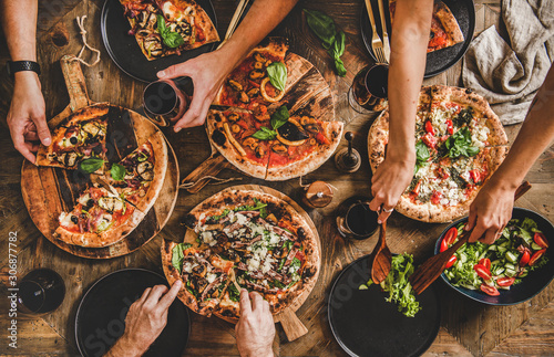 Family or friends having pizza party dinner. Flat-lay of people cutting and e...