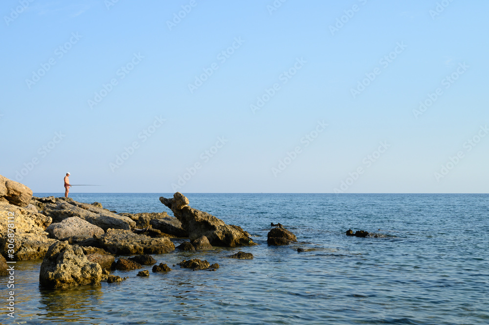 Fisherman on the rocks fishing. Seascape. Beautiful landscape with rocks, sea and clear sky. Outdoor activity in the nature
