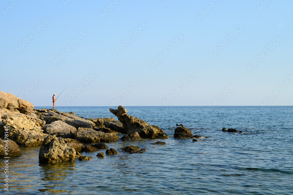 Fisherman on the rocks fishing. Seascape. Beautiful landscape with rocks, sea and clear sky. Outdoor activity in the nature