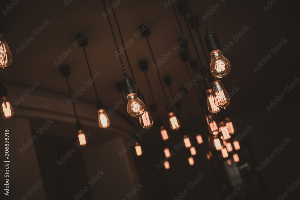 Vintage style old lamps and bulbs hanging from a ceiling in a dark moody room. 
