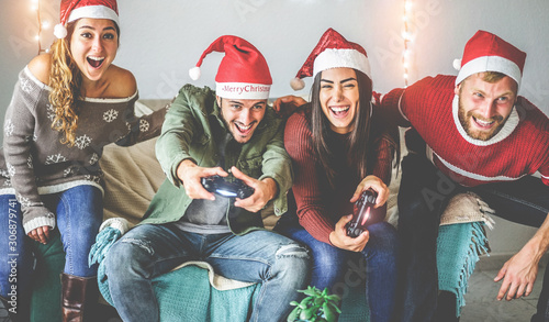 Group of happy friends having fun with video games console on christmas time - Young millennial people playing and laughing on winter holiday with vintage light on background - Focus on center guys photo