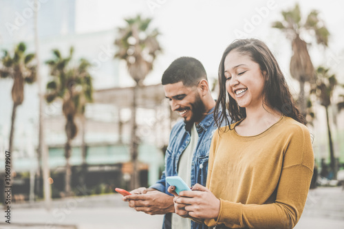 Latin couple shopping online using smartphone app - Young people having fun with new e-commerce technology trend - Social network, tech and millennial concept - Focus on girl face