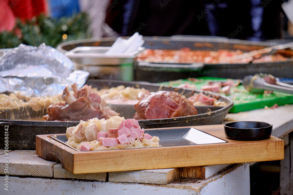 Obraz premium Focus on traditional Croatian Buncek- Pork Hock preparation in large skillet. Plated cabbage and pork from stewing preparation. Advent Market Zagreb, Croatia 