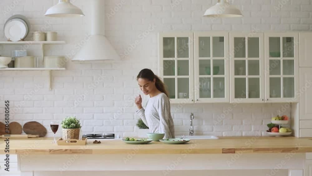 Carefree happy young woman dancing alone cooking meal in kitchen Carefree happy young woman dancing alone cooking meal in kitchen