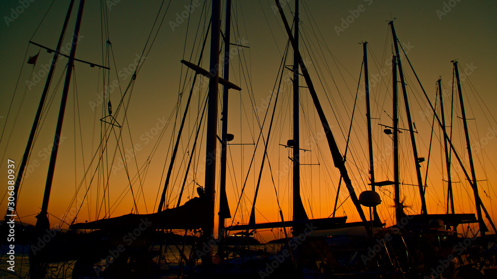 Sunset by the sea. Masts of boats in the harbor. The glare of the sun at the sea.