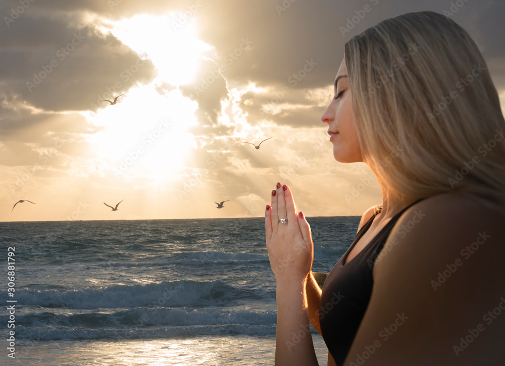 Young Adult Woman Relaxed Prayer Pose at Beach - Seagulls Orange Sunlight Sky Clouds Parting - Visual Meditation Yoga Zen - Feelings of Empowerment Concept - obrazy, fototapety, plakaty 