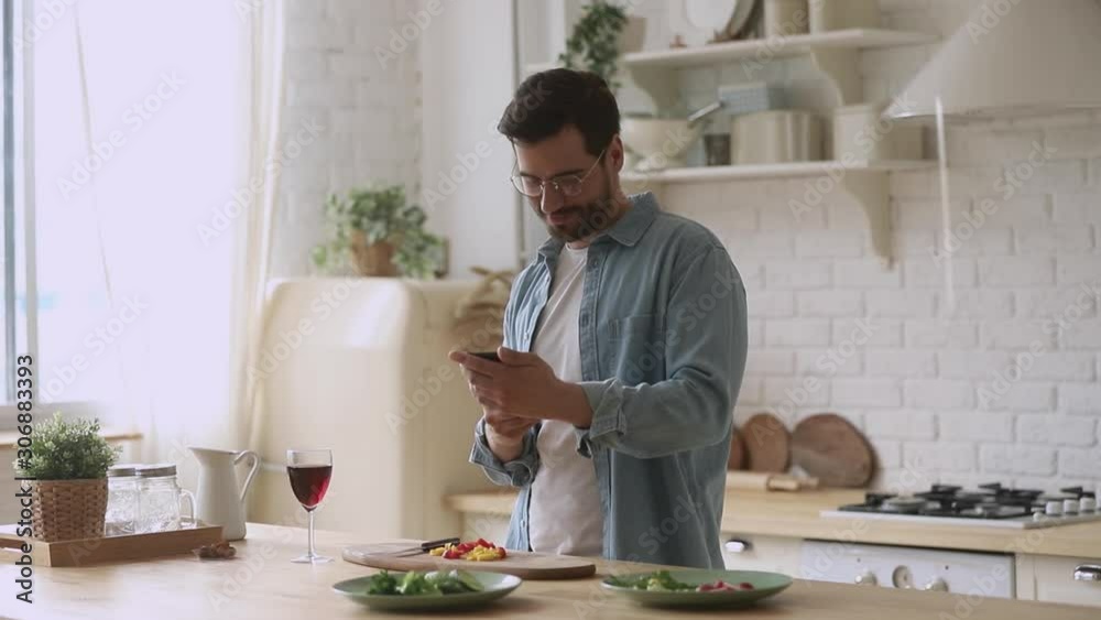 Happy young man preparing romantic dinner using smartphone mobile apps Happy young man preparing romantic dinner using smartphone mobile apps