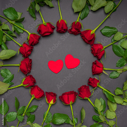 Two red hearts in round frame made of fresh rose flowers on black background. Modern style, creative composition. Love, romance, Valentine's day concept. Flat lay, top view