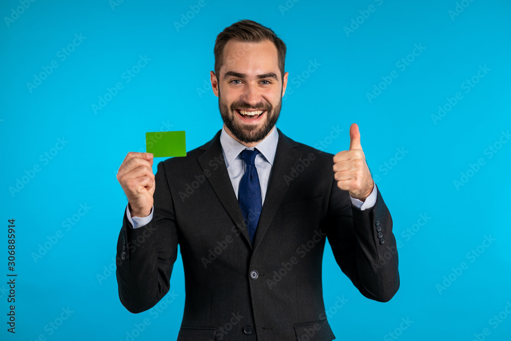 Successful man in business suit showing unlimited green credit card on blue studio background. Professional male manager. Successful man in business suit showing unlimited green credit card on blue studio background. Professional male manager.