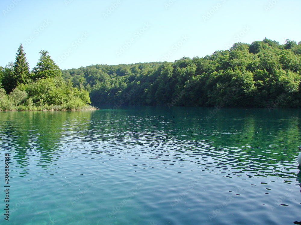 Obraz premium Enchanting combination of the colors of the untouched nature of the mountain forest against the background of the azure water surface of the lake.