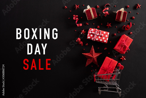 Christmas and Boxing Day background concept. Top view of shopping cart splash out Christmas decoration with gift box red star berries and ribbon on black background. photo