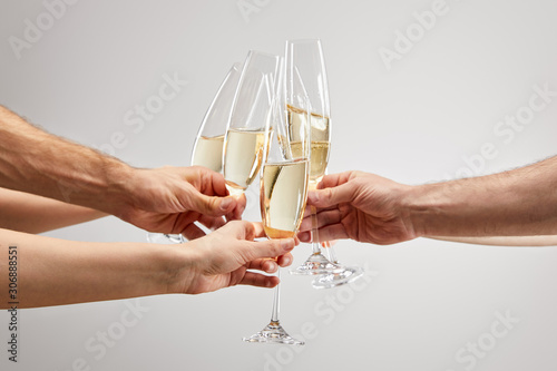 cropped view of men and women toasting while holding champagne glasses with sparkling wine isolated on grey