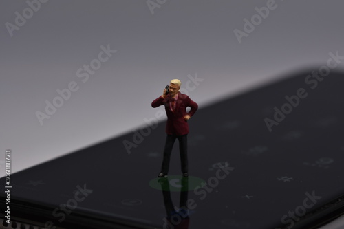 miniature man standing on a phone talking with a smartphone