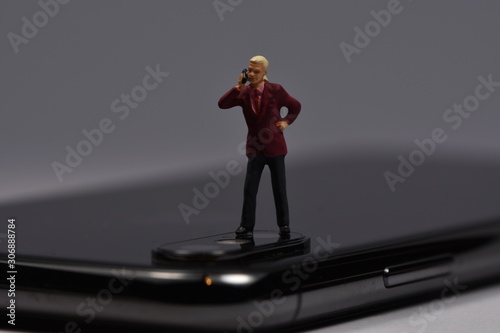 miniature man standing on a phone talking with a smartphone