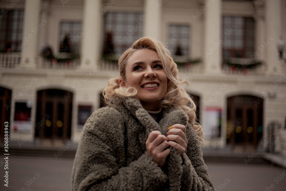 Fashion woman walking at the street, dressed modern clothes at the background the building decorated with chrictmas decorations. Female moder wearing faux fur coat, tutleneck, skirt, hat and bag Fashion woman walking at the street, dressed modern clothes at the background the building decorated with chrictmas decorations. Female moder wearing faux fur coat, tutleneck, skirt, hat and bag