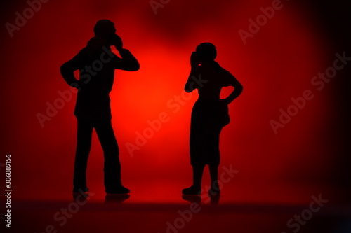 two silhouettes tiny figures with colored background talking on a mobile phone