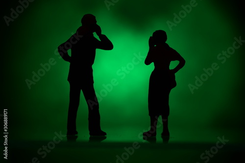 two silhouettes tiny figures with colored background talking on a mobile phone