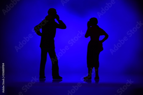 two silhouettes tiny figures with colored background talking on a mobile phone