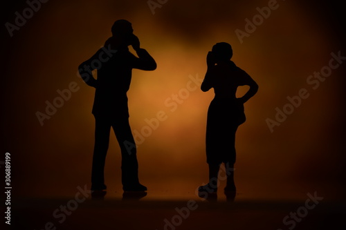 two silhouettes tiny figures with colored background talking on a mobile phone