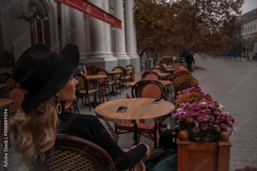 Beautiful 30s years old european woman sit in terrace of restourant and wiait the order. Female dressed black clothes and hat Beautiful 30s years old european woman sit in terrace of restourant and wiait the order. Female dressed black clothes and hat