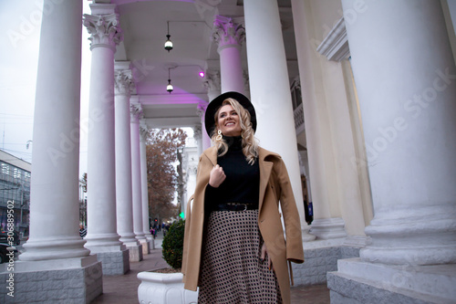Fashion woman walking at the street, dressed modern clothes. Female model wearing coat, tutleneck, skirt, hat and bag