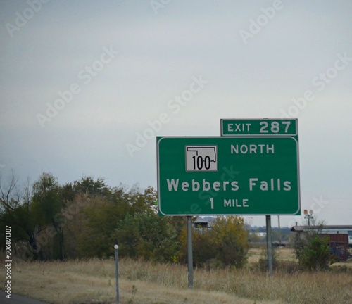 Roadside sign along the highway with directions and distance to Webbers Falls in Oklahoma.