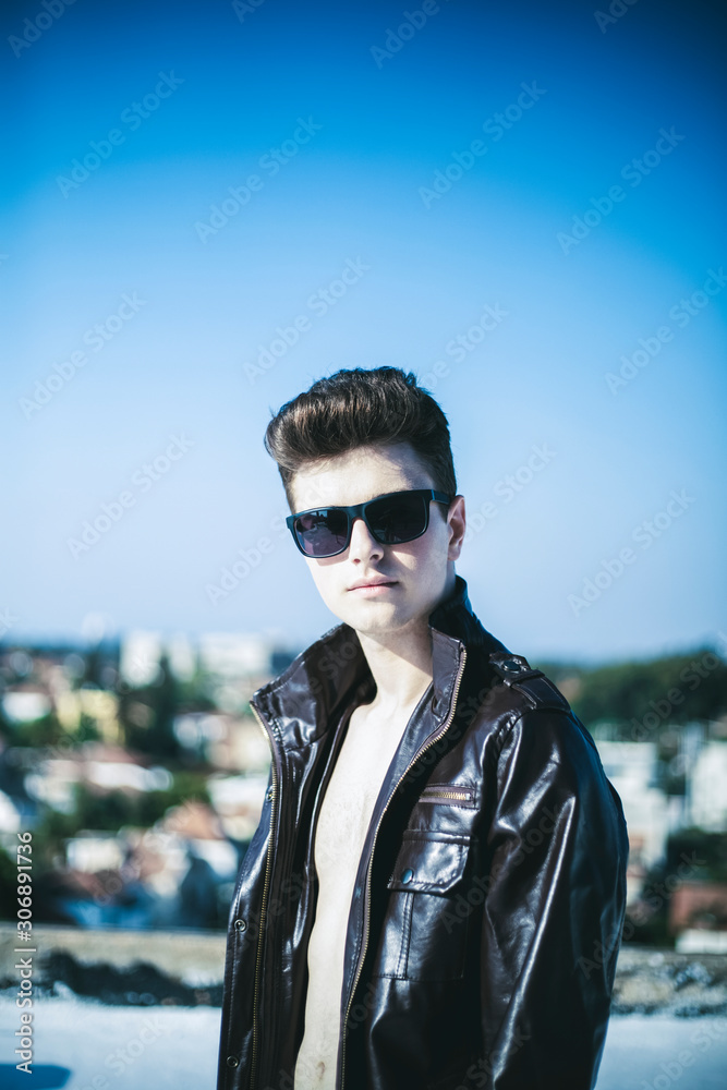 Young attractive man posing in front of camera in a dark brown jacket on the roof of a residential building Young attractive man posing in front of camera in a dark brown jacket on the roof of a residential building