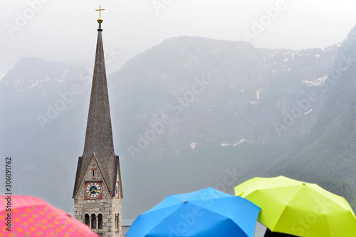 Church tower on the background of tourists umbrellas in Hallstatt.