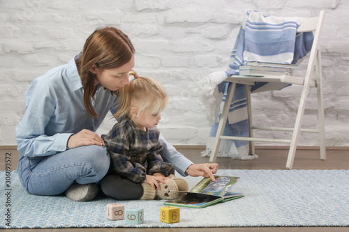 Mother and her baby girl reading a book in the nursary room photo