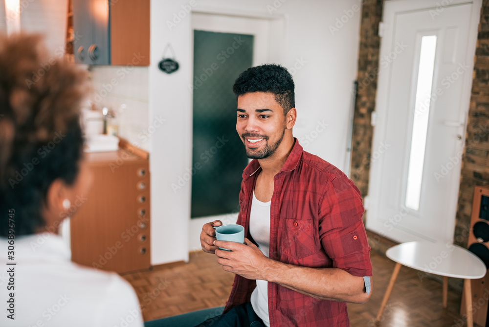 Young smiling african american man with a mug indoors, talking to a female person. Young smiling african american man with a mug indoors, talking to a female person.