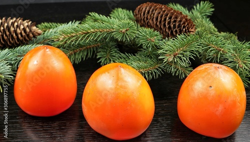 Ripe persimmon fruits, fir cones and spruce branch are on a dark wooden tableSAMSUNG CSC