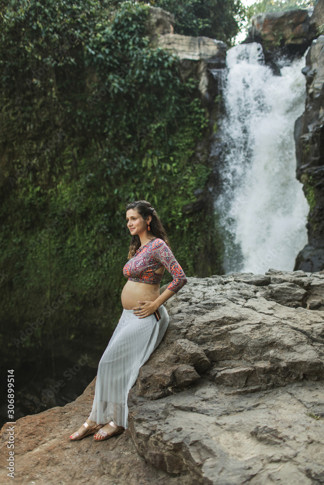 Young happy latin pregnant woman enjoying maternity and nature outdoor. Holding naked belly. Harmony with nature, childbirth in Bali travel. Spiritual maternity happiness. Young happy latin pregnant woman enjoying maternity and nature outdoor. Holding naked belly. Harmony with nature, childbirth in Bali travel. Spiritual maternity happiness.