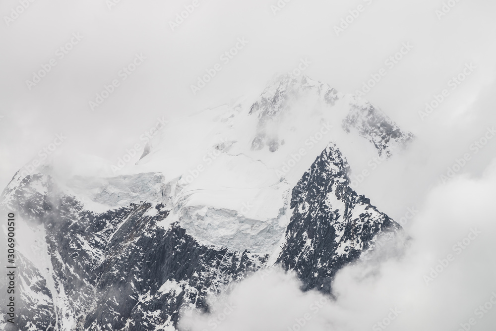 Obraz premium Atmospheric minimalist alpine landscape with massive hanging glacier on snowy mountain peak. Big balcony serac on glacial edge. Low clouds among snowbound mountains. Majestic scenery on high altitude.