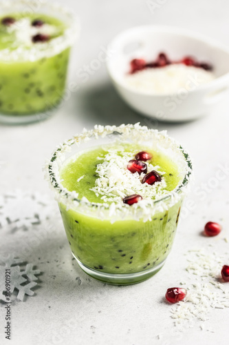 Party Christmas healthy vegetarian dessert, kiwi smoothie sprinked with coconut flakes and pomegranate seeds. Selective focus, space for text.