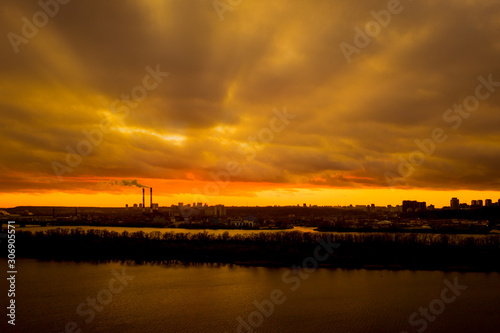 Epic sunbeams through thunderclouds in the bright sky during sunset over the city river. Sunset clouds in a sunset city over a river. © Andrii Chagovets