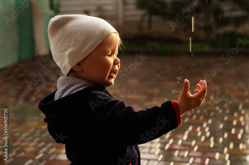 a small child catches raindrops, splashes fly into his face, closes his eyes. rainy weather. wet weather. acquaintance with the world.