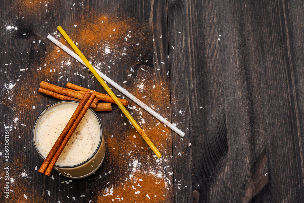 Traditional winter eggnog with milk, rum and cinnamon, sprinkle with grated nutmeg. Cocktail straws, dark wooden background Traditional winter eggnog with milk, rum and cinnamon, sprinkle with grated nutmeg. Cocktail straws, dark wooden background