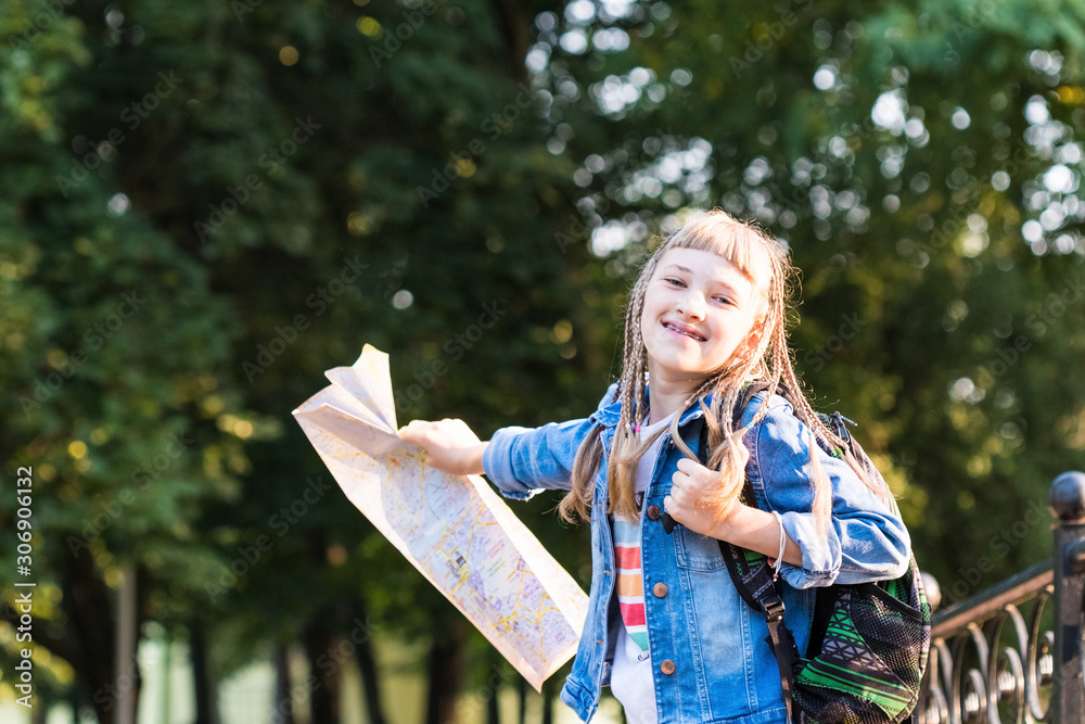 Naklejka premium Happy girl holds a paper map; a young traveler concept