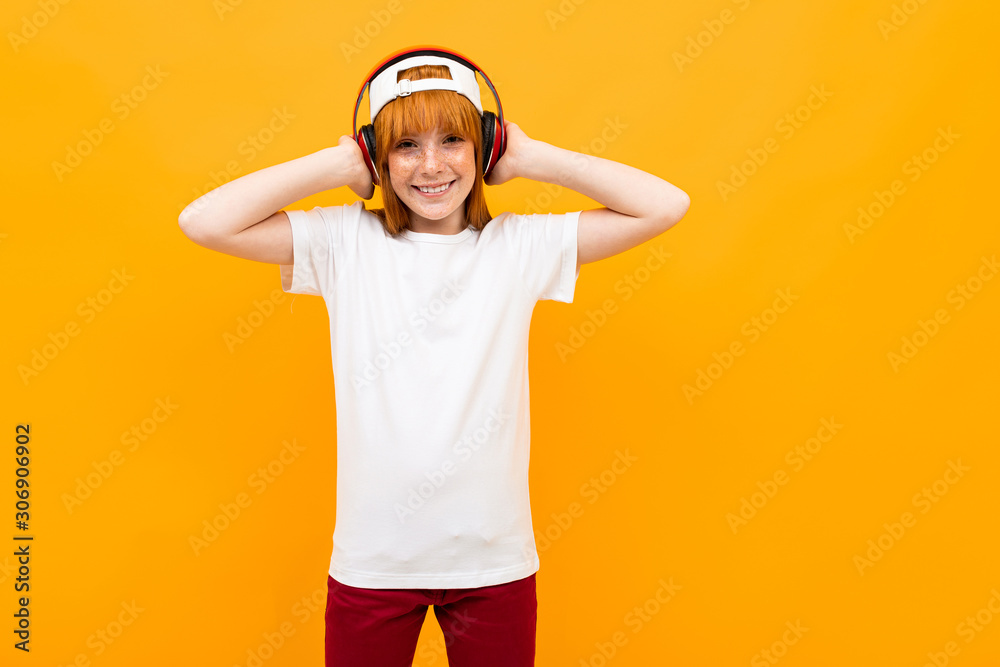 smiling european red-haired girl in a white t-shirt with a phone on a yellow background.
