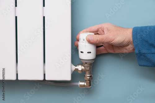 Hand turning down temperature on TRV radiator thermostat valve