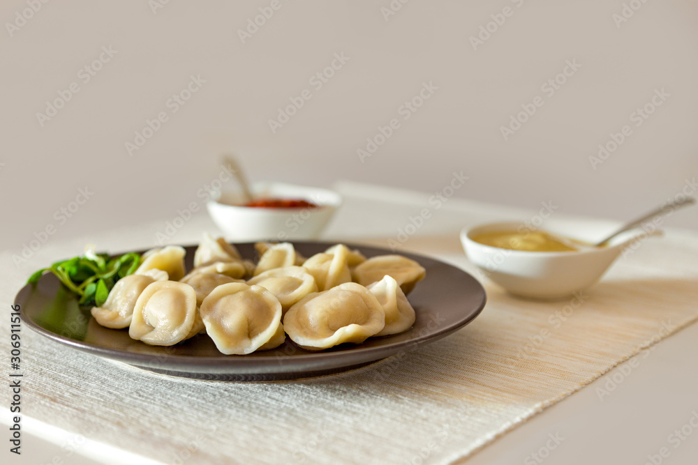 Russian food pelmeni meat dumplings with mustard and tomato sauce on a brown plate. Placed on a table with placemat.