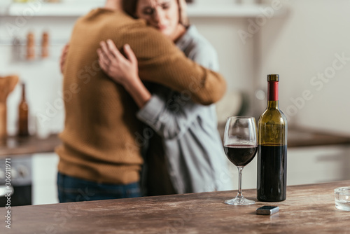 Selective focus of wine bottle and glass on table and hugging couple at background
