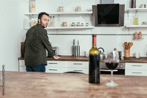 Fototapeta Naklejka Na Ścianę i Meble -  Selective focus of pensive man looking at wine on kitchen table