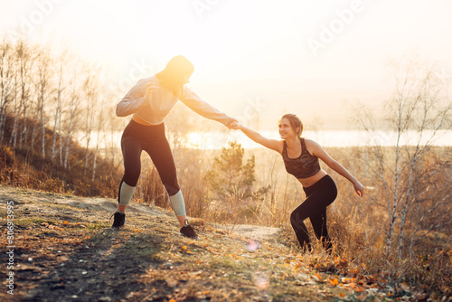 The girl reaches out to her friend. Women's mutual assistance and friendship. Joint sports in nature.